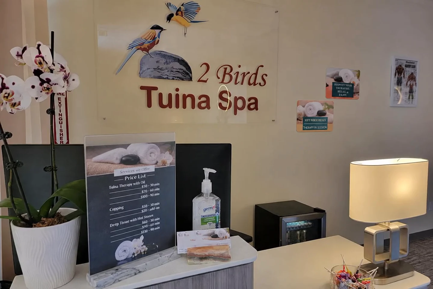 The reception at 2 Birds Tuina Spa, with its two-bird wall sign, orchids and softly lit table lamp.