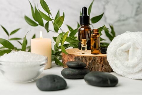A spa table with green leaves, candle, essential oils, and stones.
