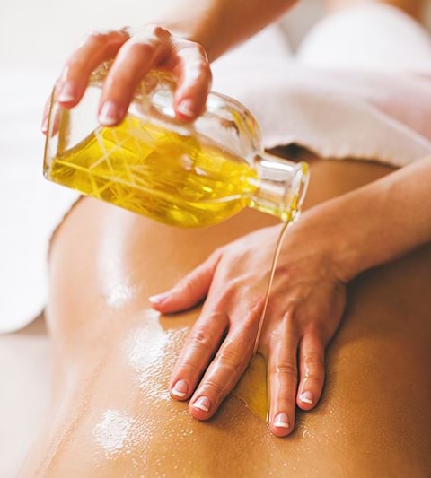 A person receiving a massage with organic oil being poured on back between the therapist's fingers.