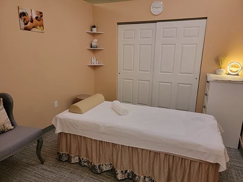 A spa room with a massage table, chair, sand light, and painting.