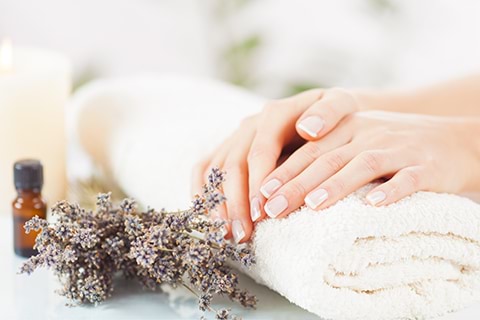 A woman getting a massage with a towel and lavender flowers, a bottle of essential oil, and a candle on the table next to her.